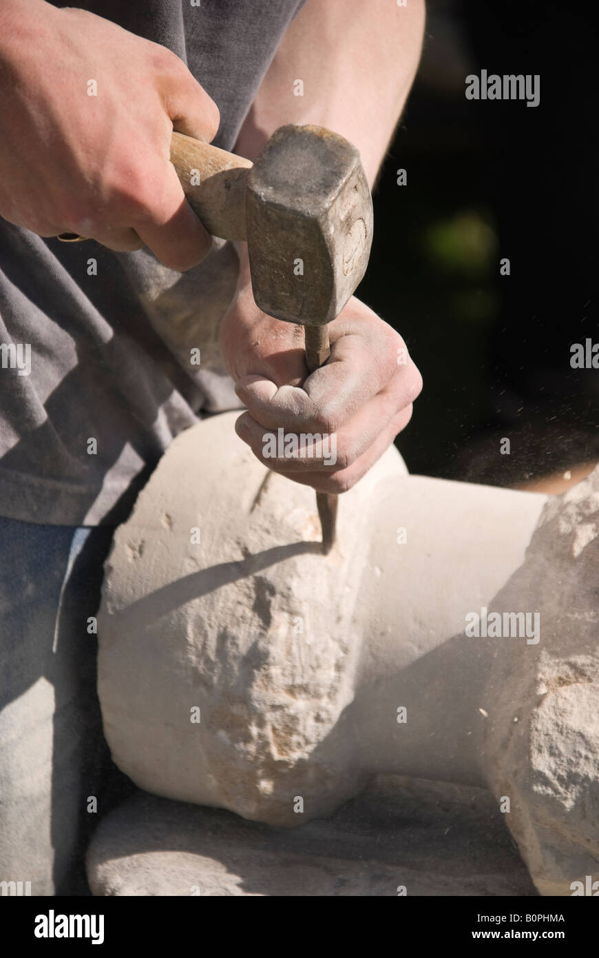 Stone mason carving a circular column with hammer and chisel Stock