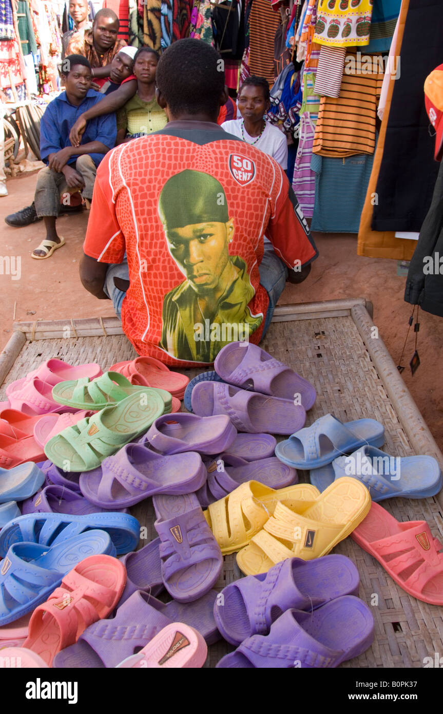 Male person with shirt printed with image of rapper 50 Cent, sitting on bed full of coloured plastic slippers. Mozambique Stock Photo