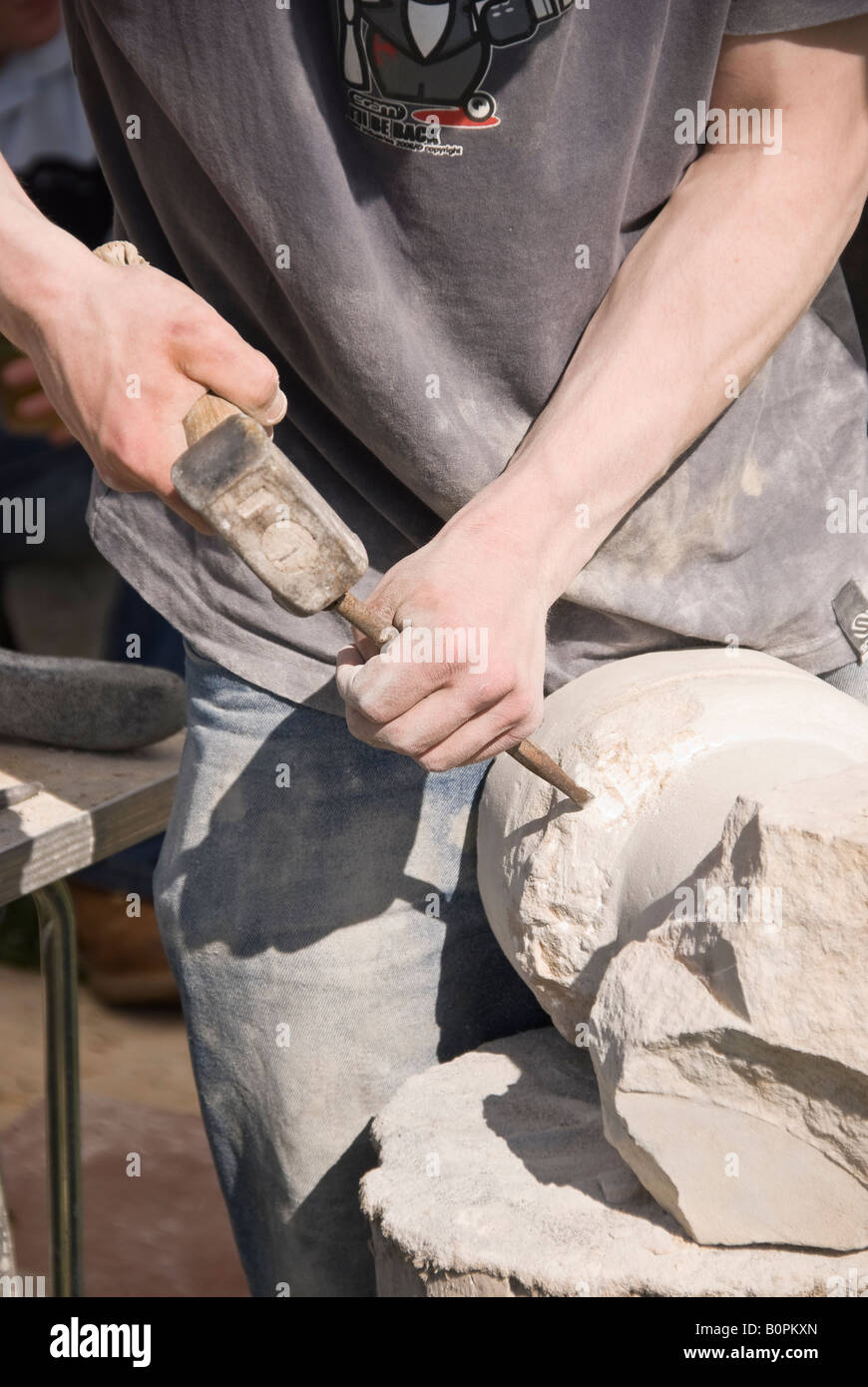 Stone mason carving a circular column with hammer and chisel Stock