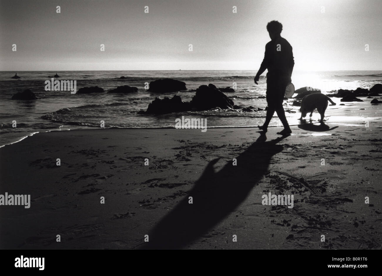 silhouette of man walking dog by the ocean black and white Stock Photo
