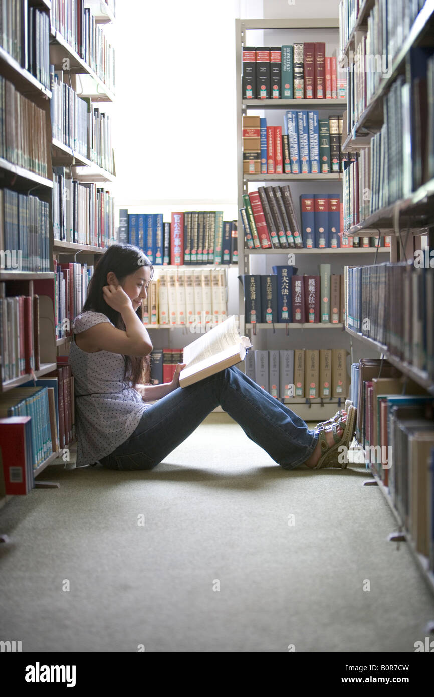 Young woman sitting on floor in library reading book Stock Photo - Alamy