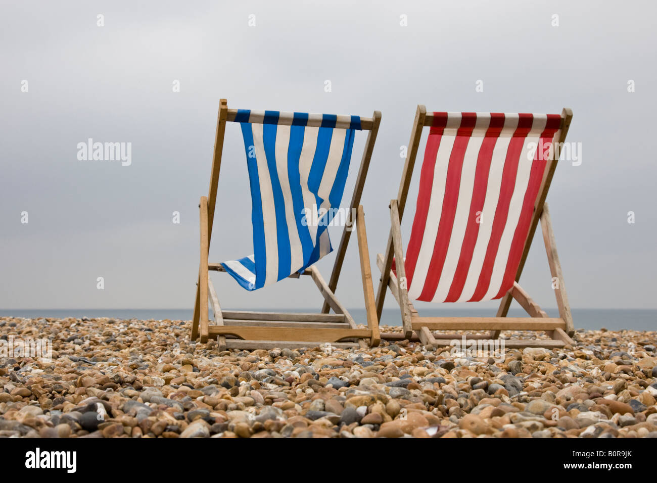 Red and blue deckchair lie empty on a british beach on a windy day out of season in the summer holidays Stock Photo