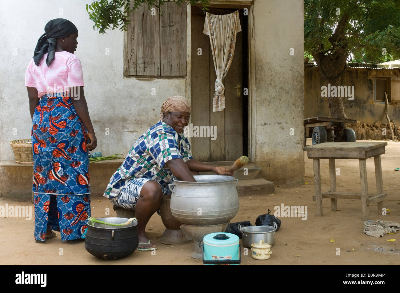 Woman cooking outside in front of her house while chatting with her neighbour, Kuluedor, Ghana Stock Photo