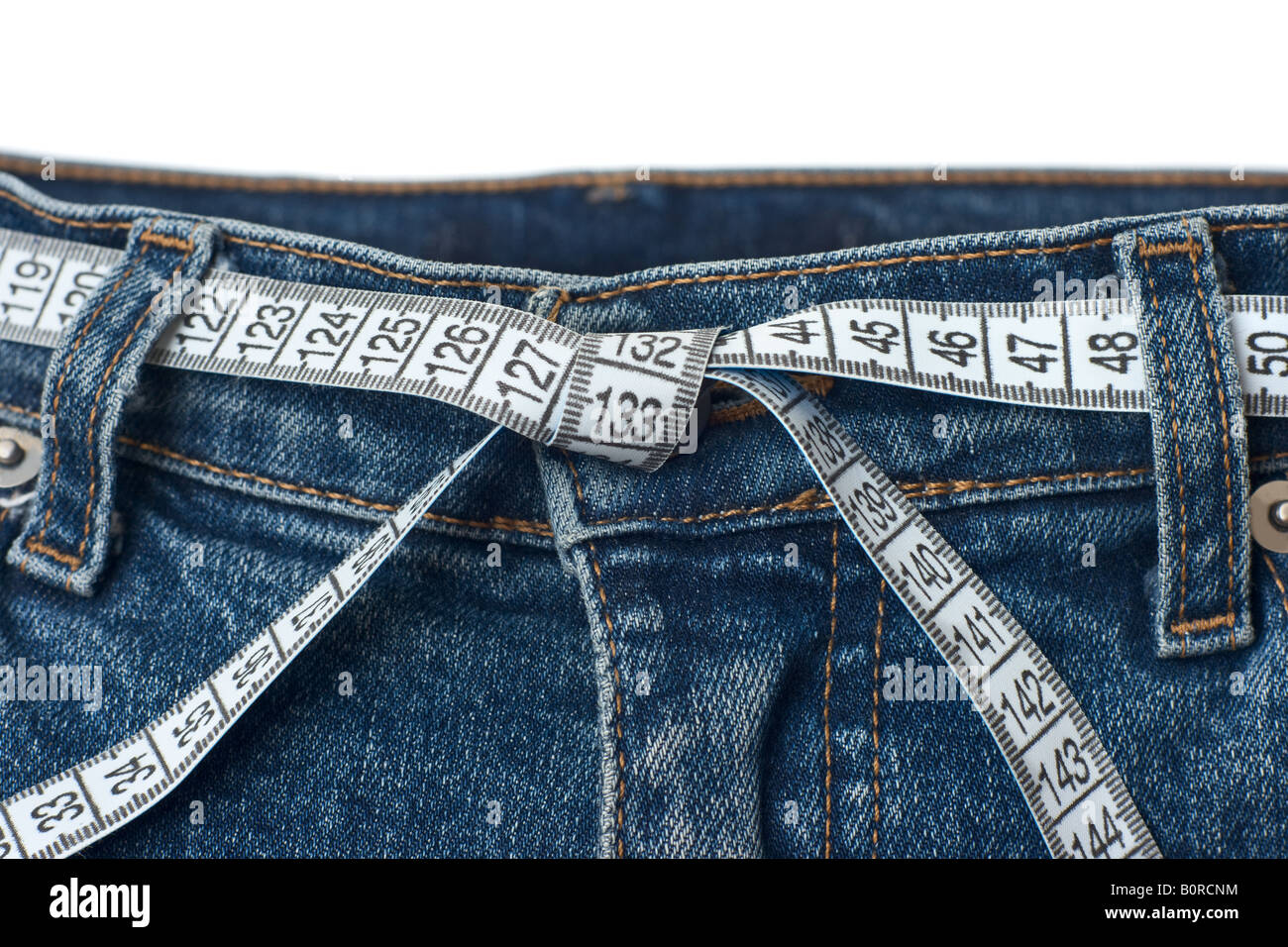 Waist check and excess weight control.  Pair of blue jeans with measuring tape as belt having tied knot isolated on white Stock Photo
