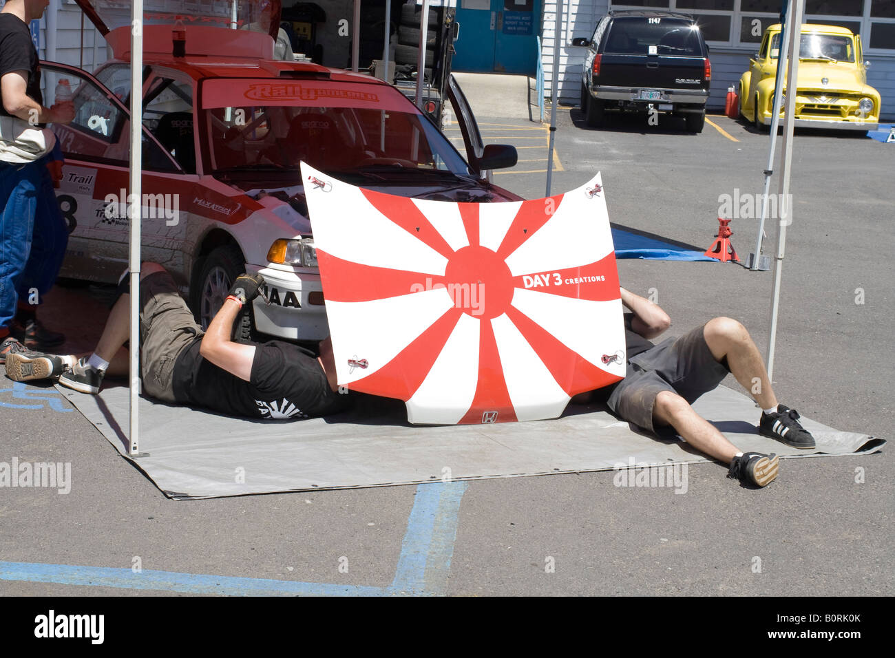 Rally service crew members use their car's hood to hide from the sun Stock Photo