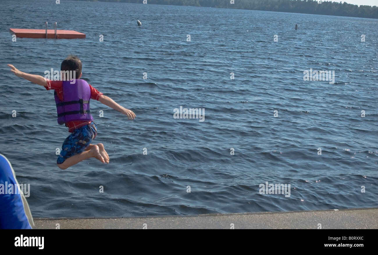 young boy leaps from waterfront dock at summer hotel camp Stock Photo