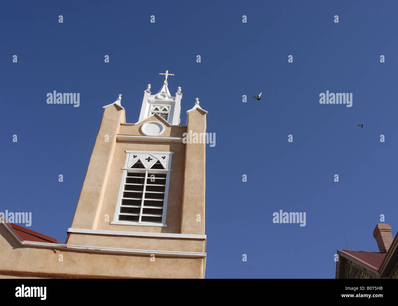 Pigeons land on one of the towers at San Felipe de Neri Catholc Church in the old town area of Albuquerque New Mexico Stock Photo