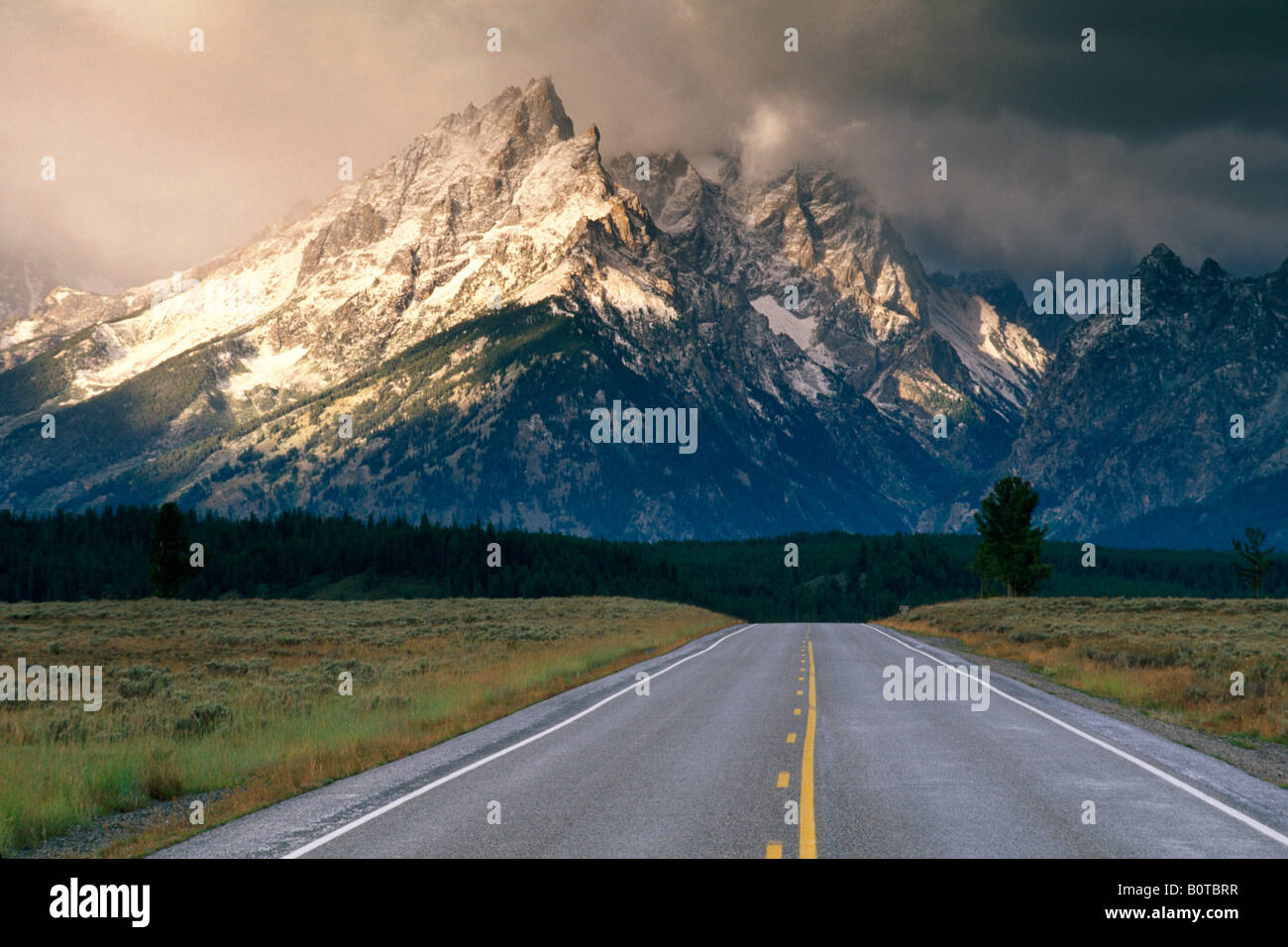 Straight road below mountain range dusted by first snow of fall Grand Teton National Park WYOMING Stock Photo