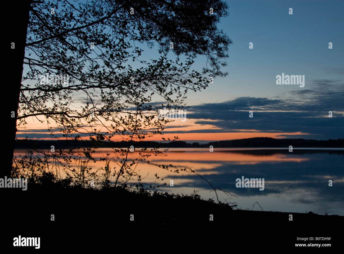 Lake surface mirroring the colourful sky after sunset Stock Photo