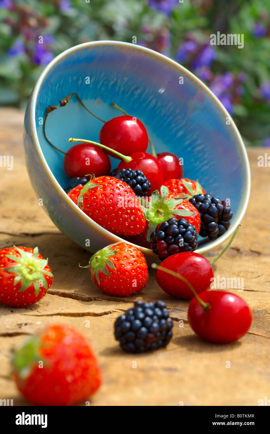 bowl of fresh picked summer soft fruit on a wooden garden table, cherry, strawberry and blackberry Stock Photo