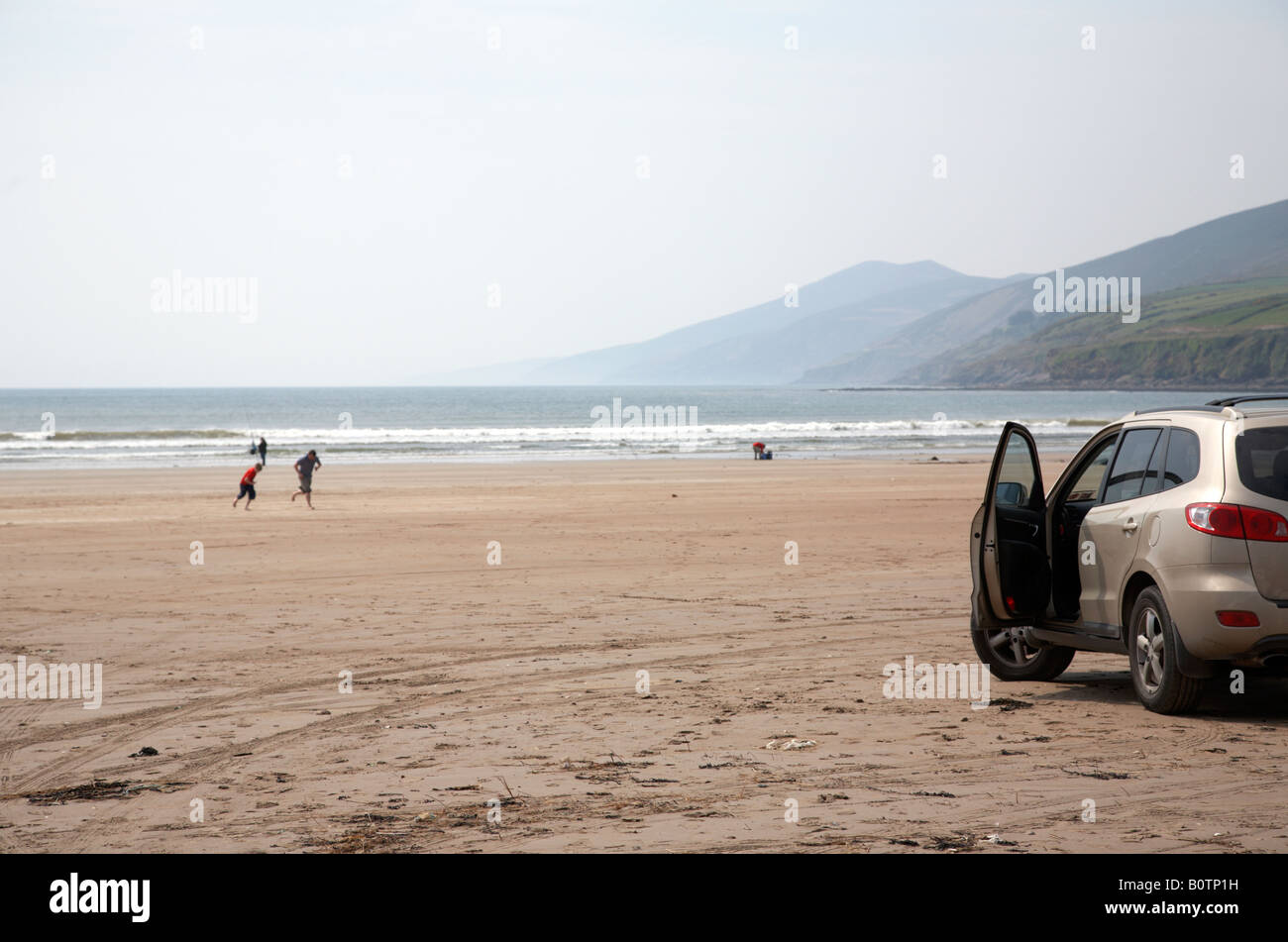 car parked on the beach with door open as people enjoy inch strand