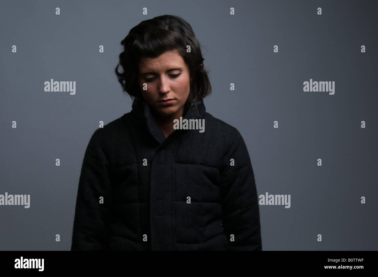 sad lonely depressed young woman girl standing with shoulders slumped, moody low key lighting Stock Photo