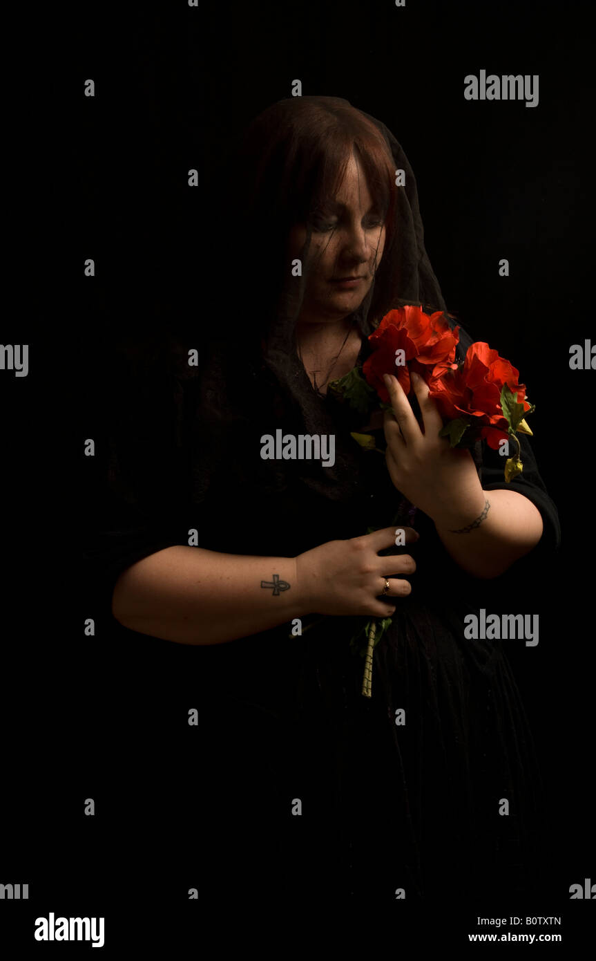 young woman dressed in black mourning clothes as if for a funeral holding bunch of red flowers