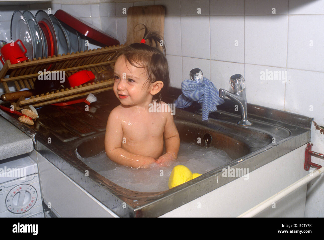 Baby girl sitting in kitchen sink, London UK Stock Photo Alamy