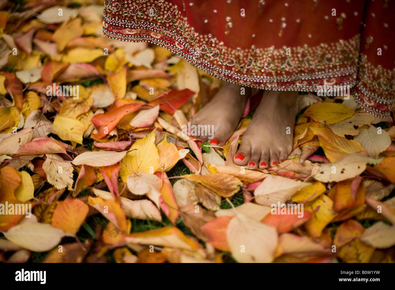 Feet of a Pakistani woman 30s wears traditional clothing in a garden with autumn leaves Stock Photo