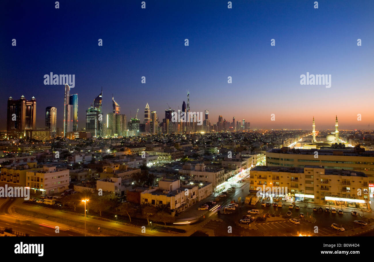 Elevated view towards the skyscrapers on Sheikh Zayed Road (L) and a mosque illuminated at dusk in Dubai, United Arab Emirates. Stock Photo