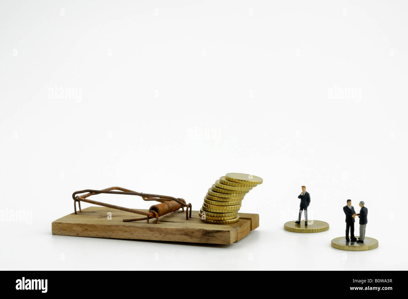 Figurines, models of businessmen beside a set mousetrap with a stack of coins as bait Stock Photo