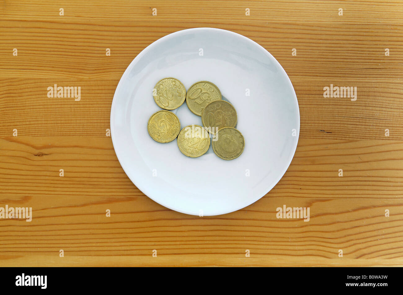 Euro coins on a white plate on a wooden table, payment for toilet use Stock Photo