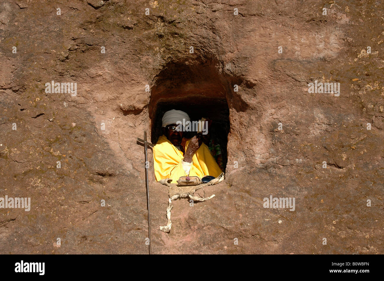 Old hermit dressed in a yellow cape praying in a small cave church hewn out of rock, Lalibela, Ethiopia, Africa Stock Photo