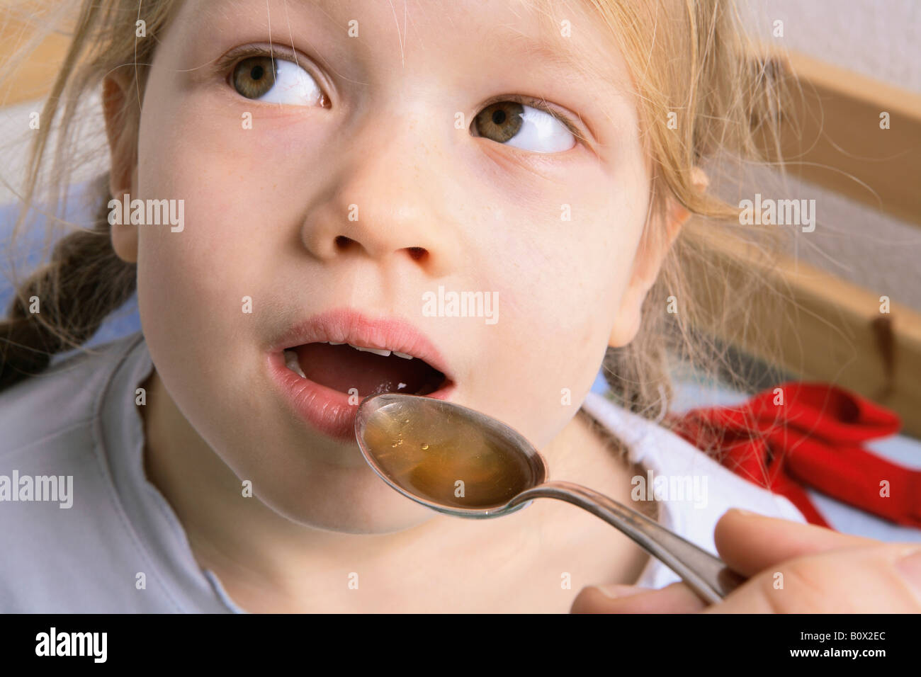 A human hand holding a spoonful of medicine for a young girl to swallow Stock Photo