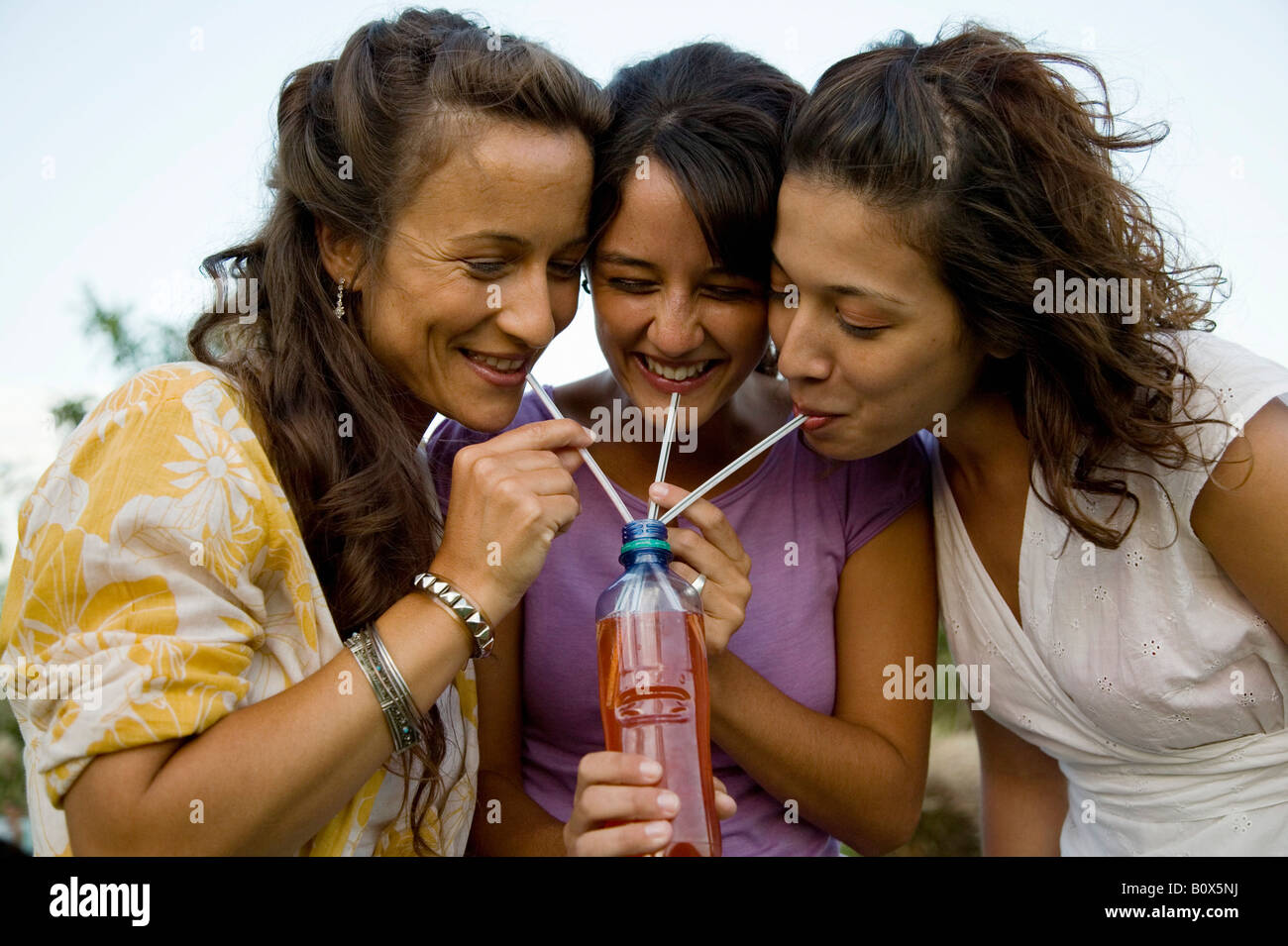 Three women drinking through straws from a bottle Stock Photo Alamy