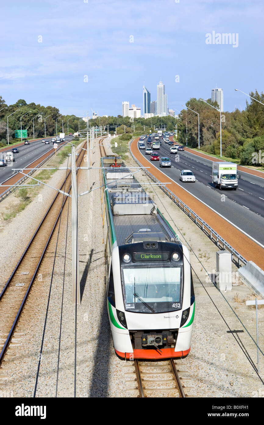 A Transperth electric train next to the Mitchell Freeway, Leederville with Perth's skyscrapers in the distance Stock Photo