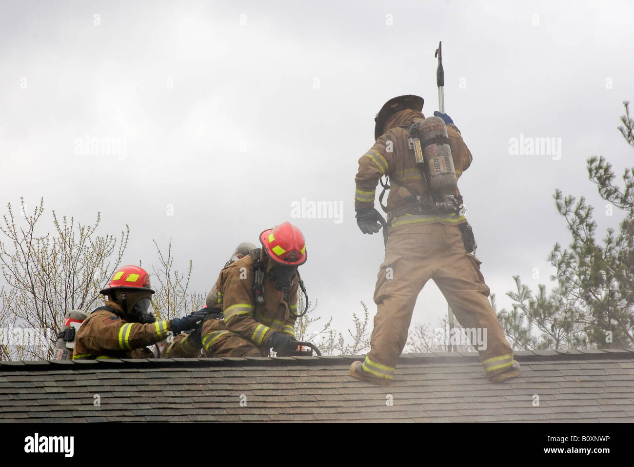 Firefighter trainees cut a hole in the roof of a burning house Stock Photo