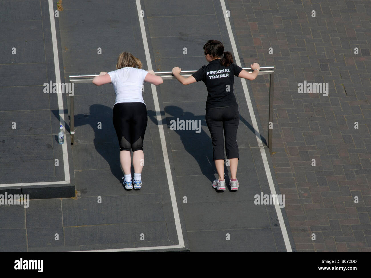 Personal trainer (indicated on the back of her t-shirt) and client doing push ups on raised bar, South Bank, London, England Stock Photo