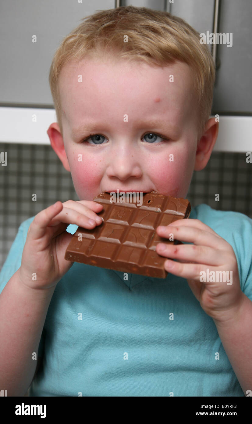 3 year old plump male child eating a large chocolate bar Stock Photo