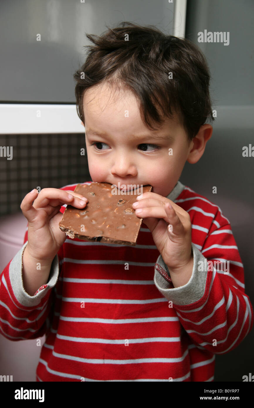 Tot sitting on kitchen side eating a large piece of chocolate to keep quite Stock Photo