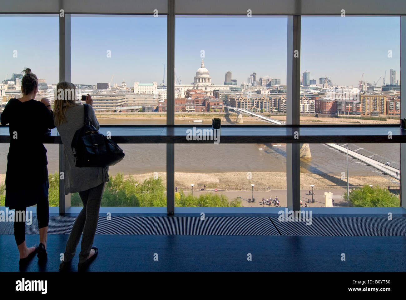 Horizontal wide angle of girls enjoying the view through a large window of London towards St Paul's Cathedral on a sunny day. Stock Photo