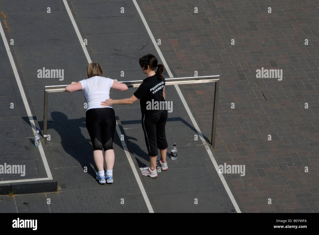 Personal trainer (indicated on the back of her t-shirt) touching back of client doing push ups on raised bar, South Bank, London Stock Photo