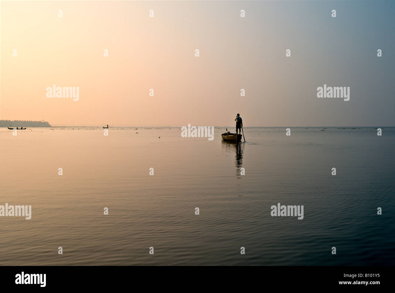 INDIA KERALA Indian fisherman poling his wooden boat in Vembanad Lake at sunset as he sets out to spend the night fishing Stock Photo