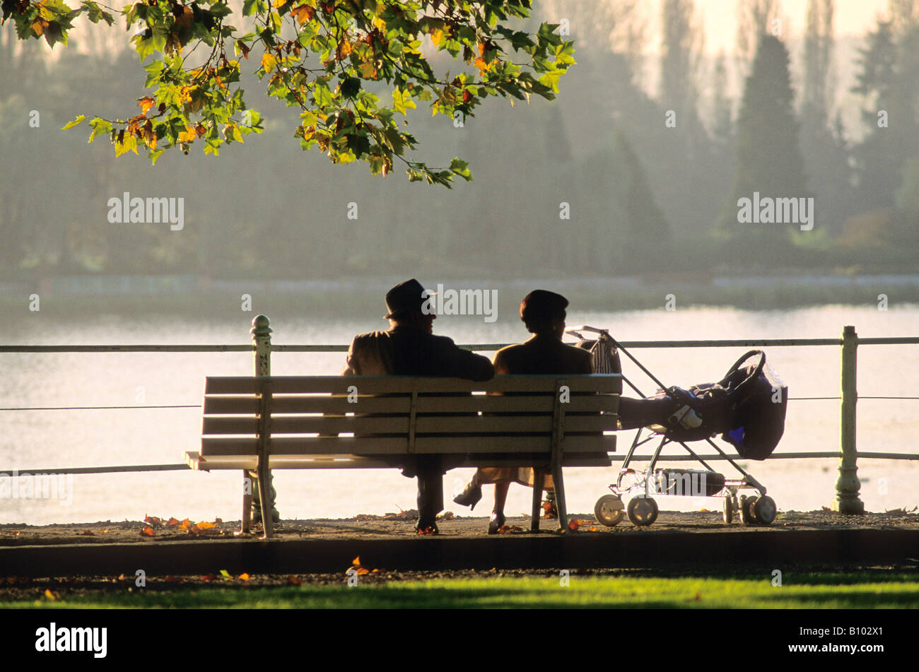 Grandparents resting on a park bench with their grandchild in a pram Stock Photo