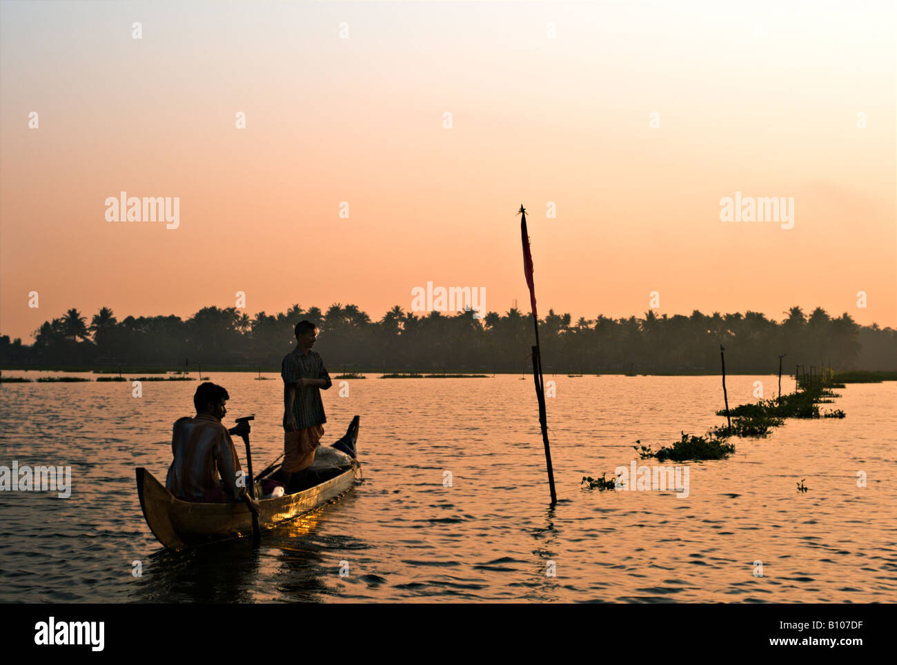 INDIA KERALA Two Indian fishermen rowing their wooden boat in Vembanad Lake at sunset as they set out to spend the night fishing Stock Photo