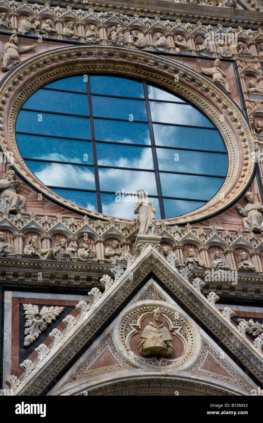 Closeup facade of the Duomo of Siena, detail view with Clouds reflected in rose glass window behind Giovanni Pisano sculptures of slain apostles. Stock Photo