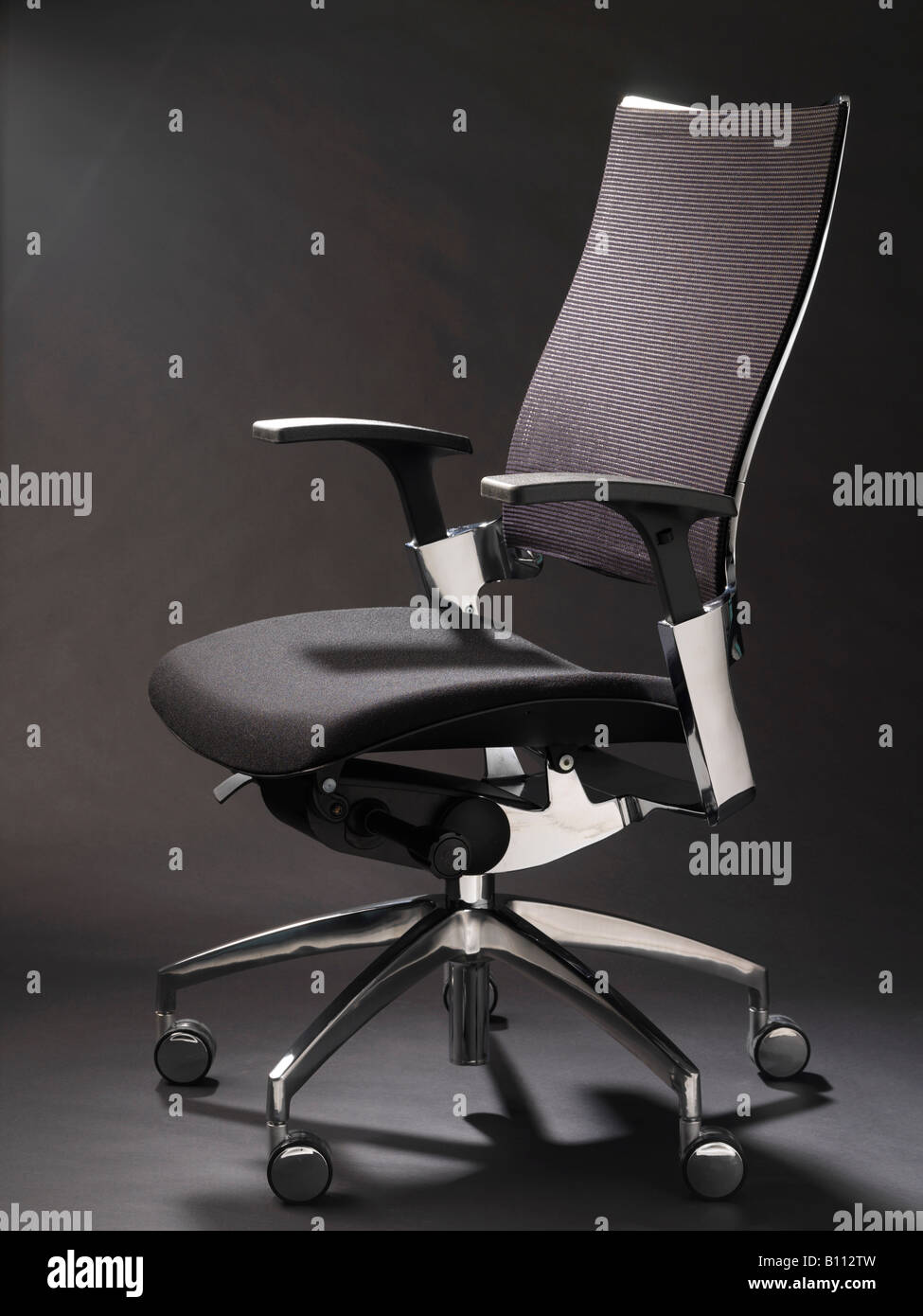 Black office chair with black arms and chrome feet on a black background Stock Photo