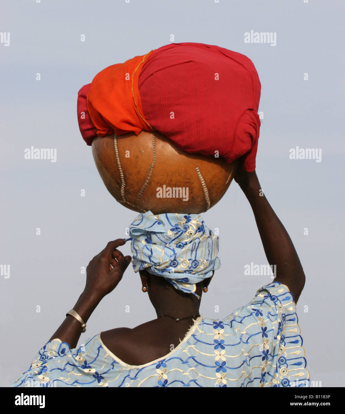 African lady carrying a calabas with clothes on her head Stock Photo
