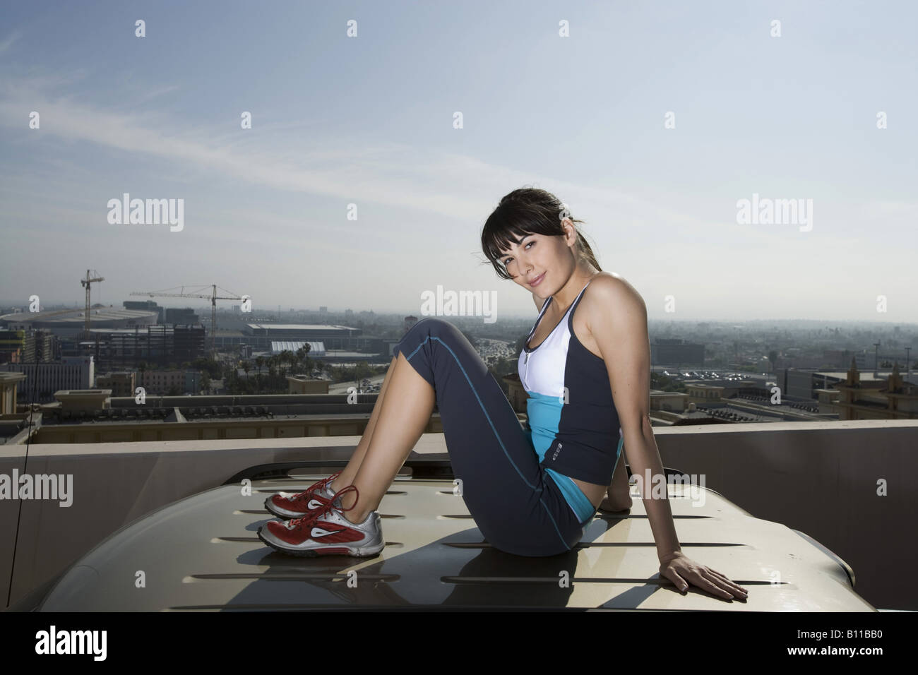Woman sitting on top of SUV on roof top car park Stock