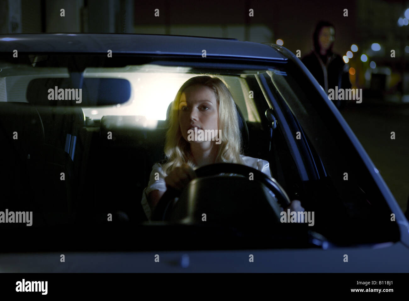 Woman in SUV views a prowler in rear view mirror at night Stock Photo