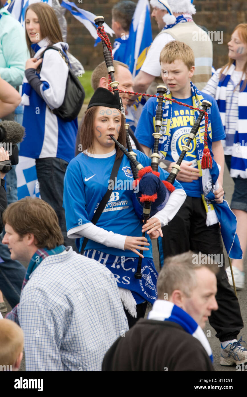 Scottish female football fan bagpiper playing the bagpipes busking at