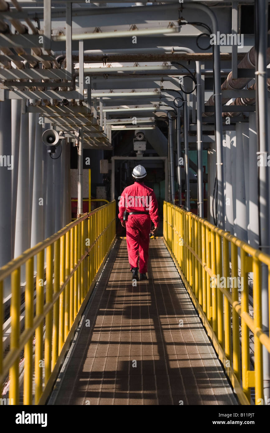 Worker crosses a bridge between two platforms under Pipework on oil and gas production rig South China Seas Indonesia 2005 Stock Photo