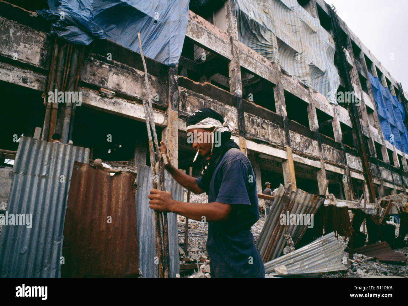 A worker smoking and holding rusted tubes in a half constructed building in Indonesia Stock Photo