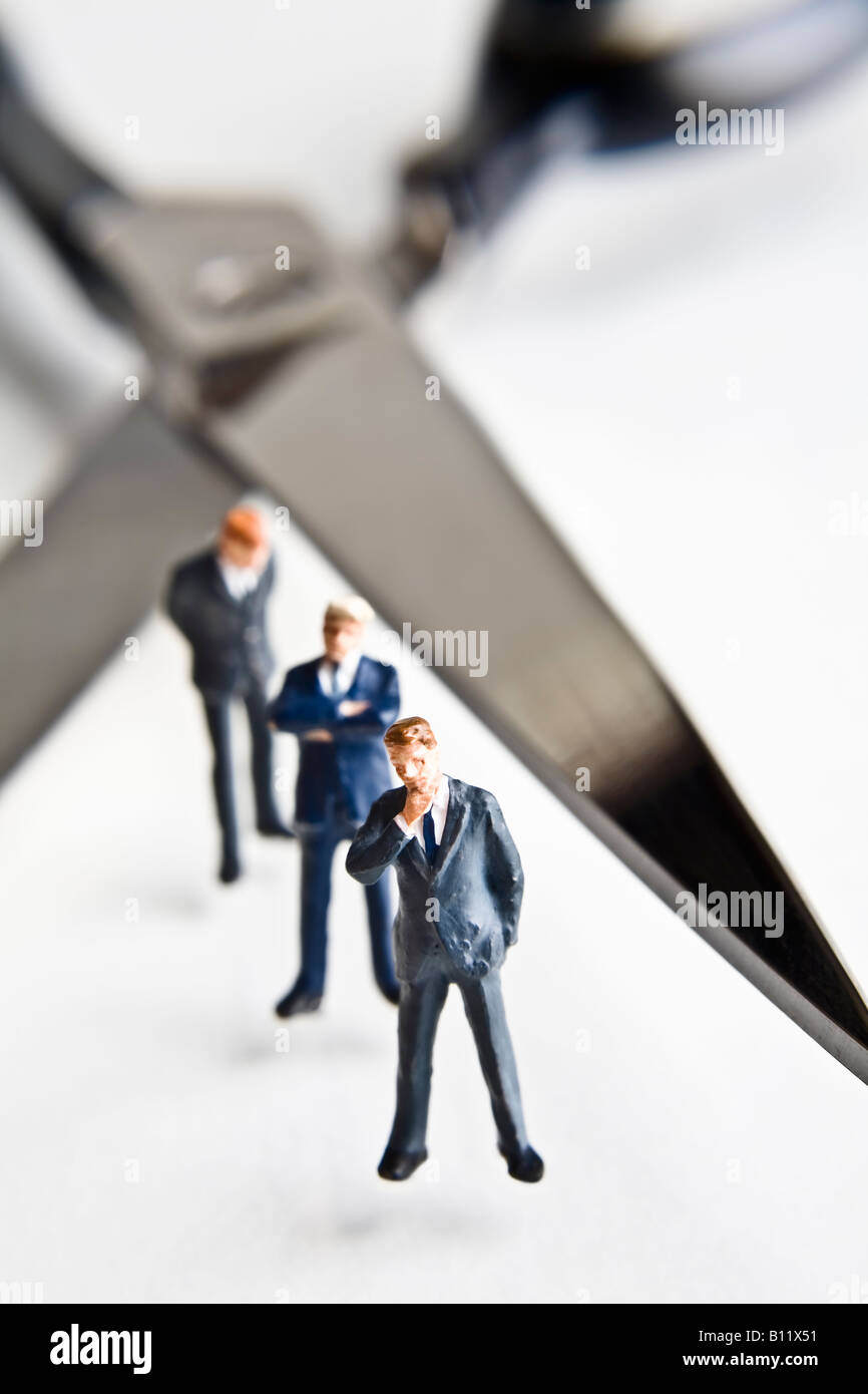 Businessman figurines standing next to scissors Stock Photo