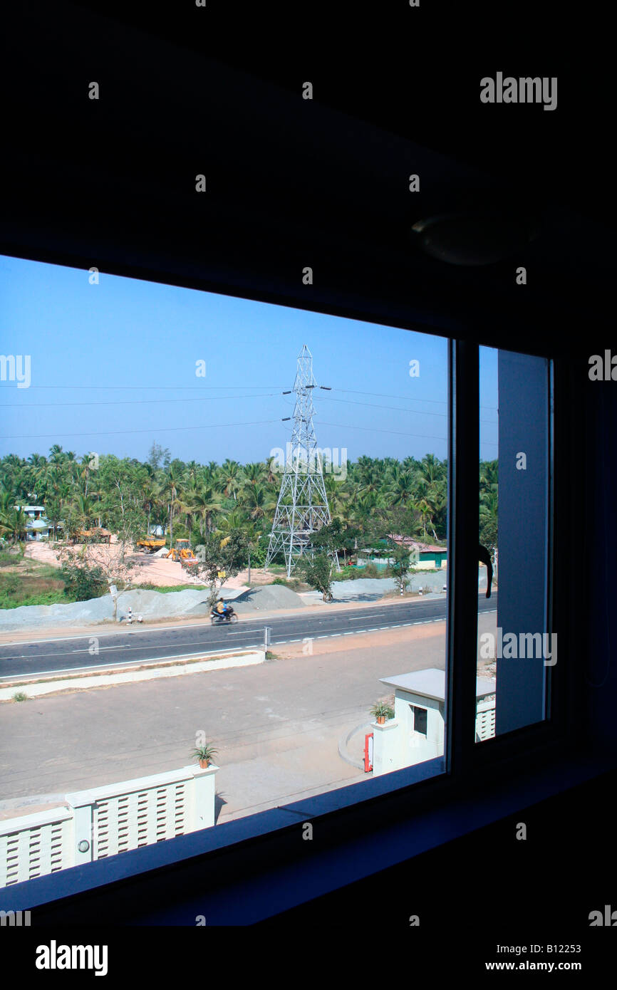 Hotel room with view of road wall gate electric pylon coconut palms trees and bright blue sky Stock Photo