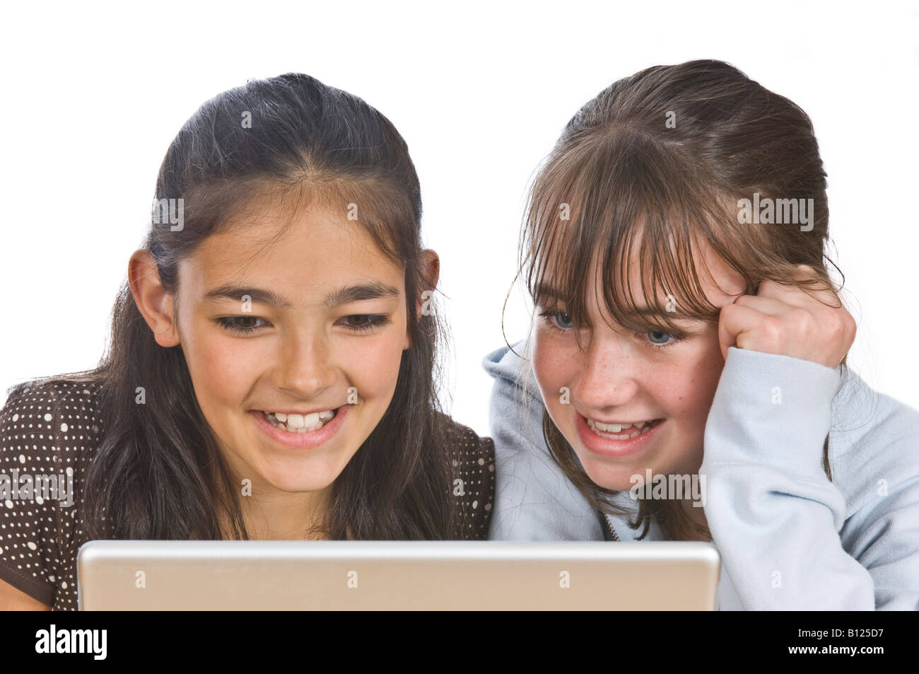 Two young girls (10 yrs) best friends looking at a lap top computer screen and smiling against a pure white (255) background. Stock Photo