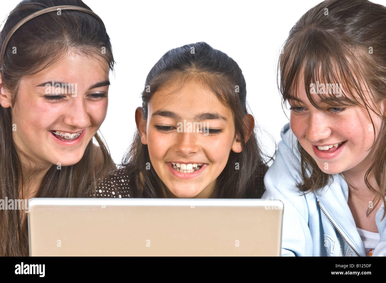 Three young girls (10 - 13 yrs) best friends looking at a lap top computer screen and laughing with one wearing a teeth brace. Stock Photo