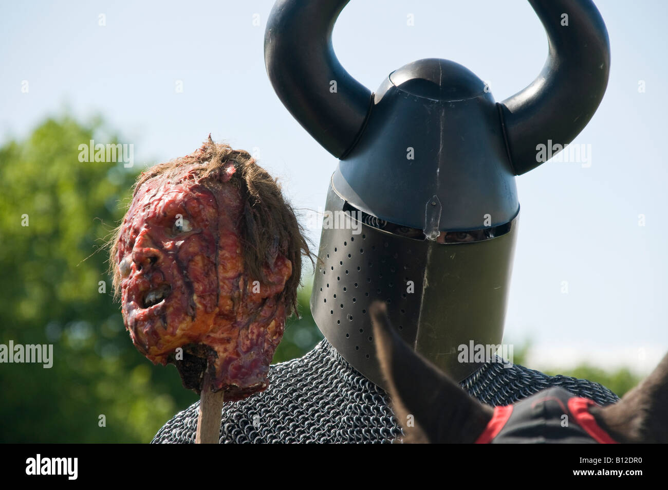 Medieval Knight wearing horned helmet, carrying a pole with a decapitated head. Stock Photo