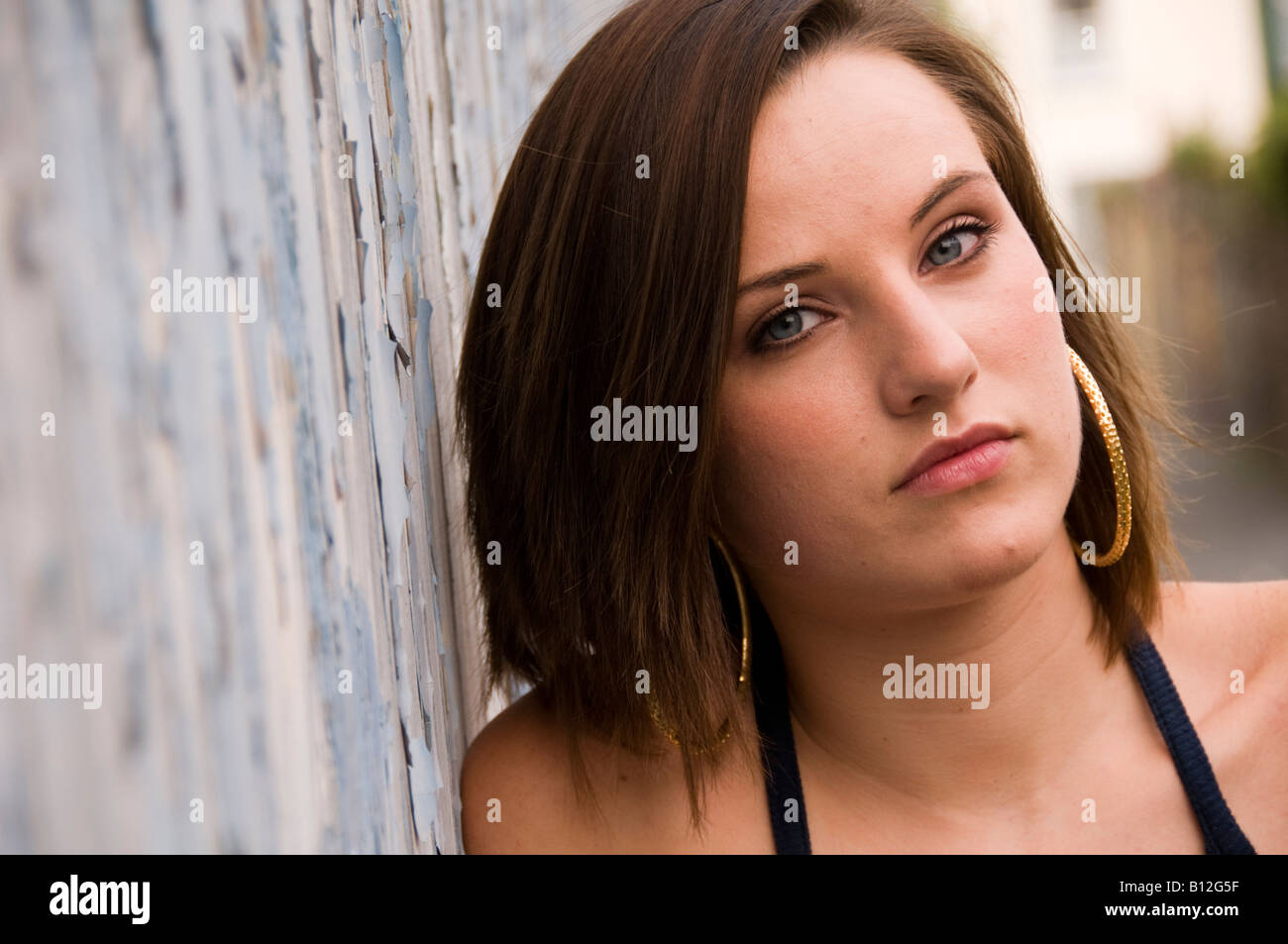 Young 19 year old Teenage girl leaning on peeling blue painted wooden wall looking moody, wales UK Stock Photo