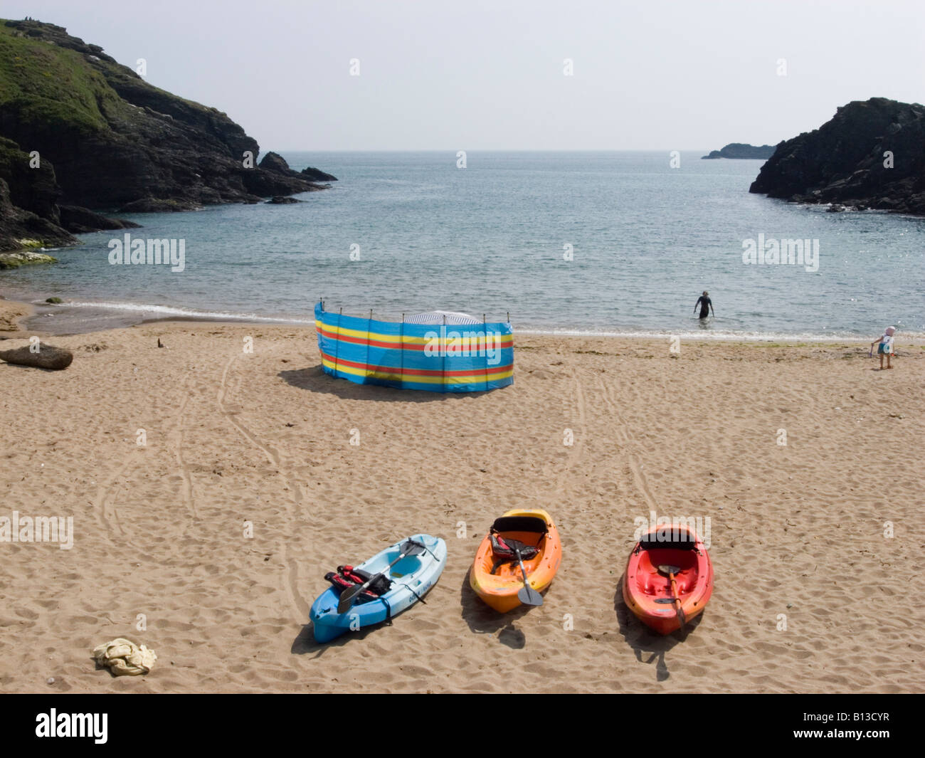 Three colourful canoes and a windbreaker on a sandy beach. Soar Mill Cove, South Hams, South Devon. UK Stock Photo